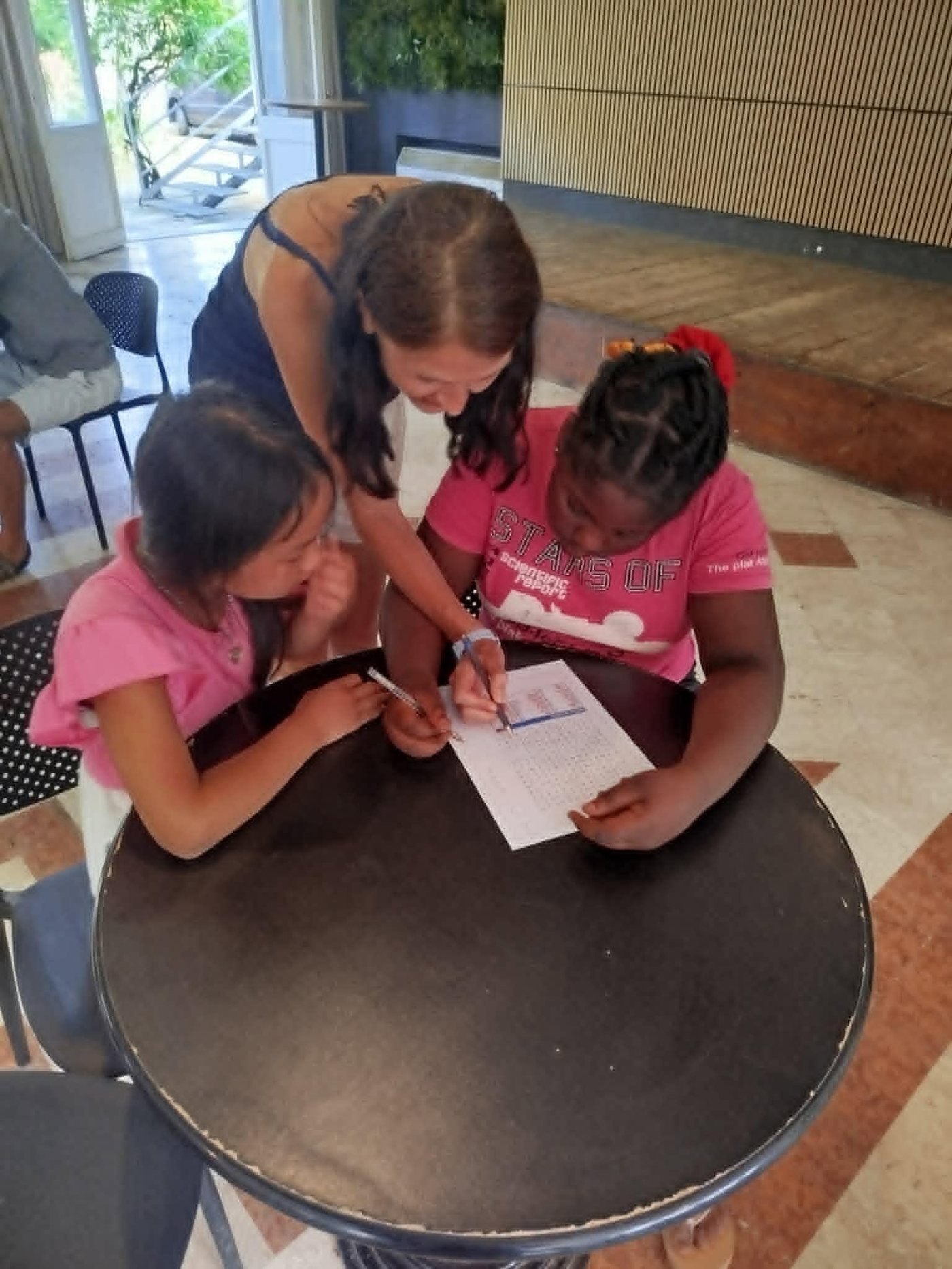 Bambine e un'educatrice attorno a un tavolino, concentrate su un gioco di parole