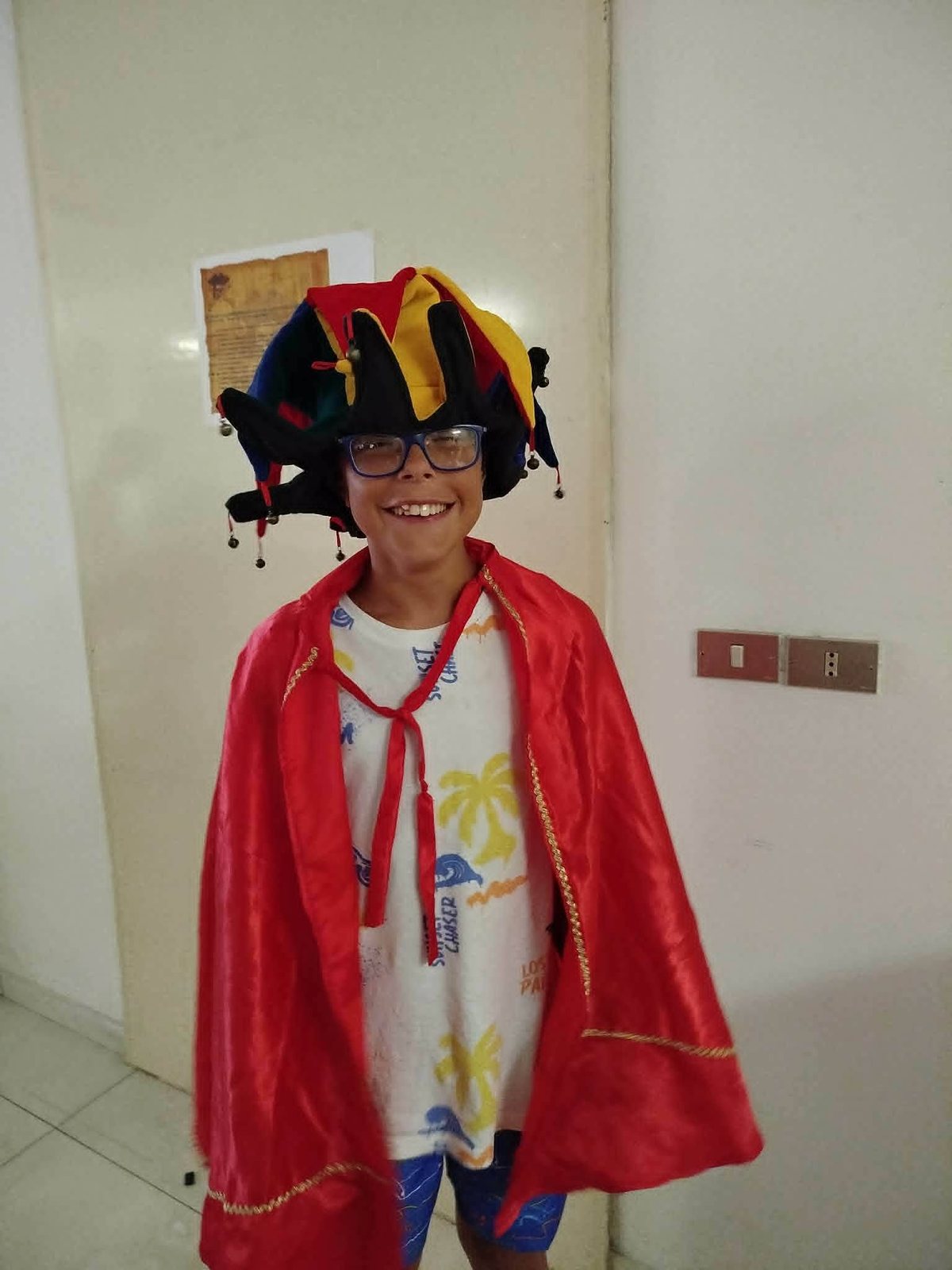 Un bambino con mantello rosso e cappello da giullare, pronto per la serata a tema