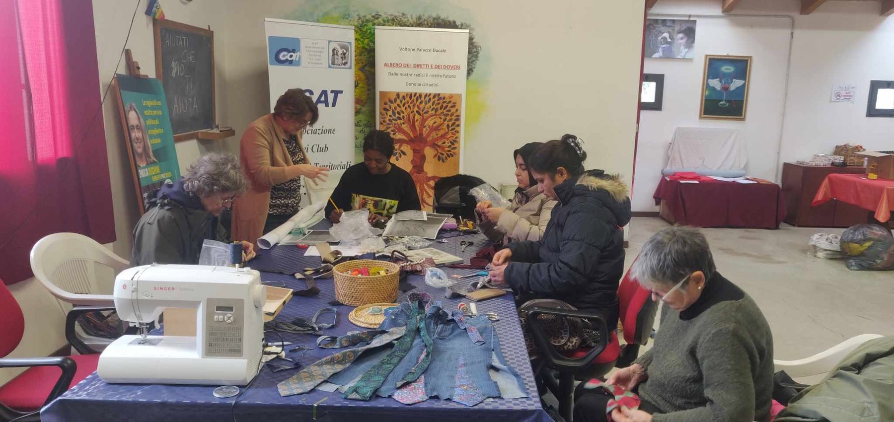 Il gruppo di sartoria di Ubuntu lavora attorno a un tavolo con tessuti e macchine da cucire